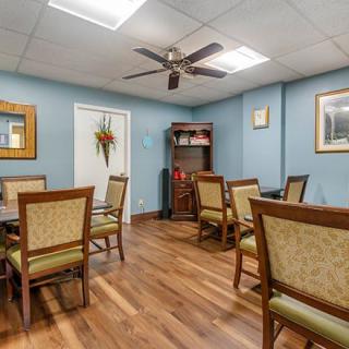 A cozy dining area with wooden flooring, featuring several tables and chairs, ceiling fan, and blue-painted walls adorned with decorations.
