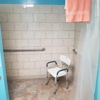 An accessible shower stall with a shower chair and grab bar.