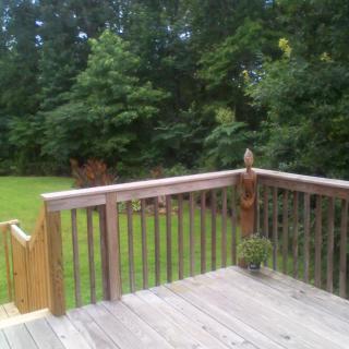 A wooden deck overlooking a lush backyard with green grass and trees.