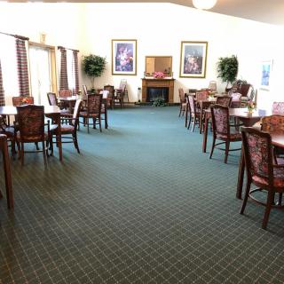An indoor dining area featuring several tables and chairs, with decorative plants and paintings adorning the space.