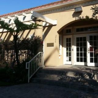 A sunlit entrance to a building with arched windows and shadow patterns from surrounding foliage.