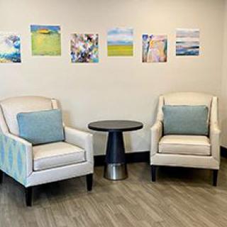 A cozy waiting area with two upholstered chairs, a round side table, and vibrant artwork on the wall.