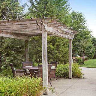 A serene outdoor seating area under a wooden pergola, surrounded by lush greenery.