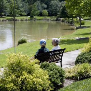Two people sitting on a bench by a lake in a park, enjoying a peaceful day outdoors.
