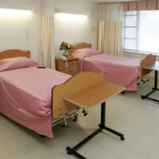 A clean and well-lit hospital room with two beds and accompanying furniture.