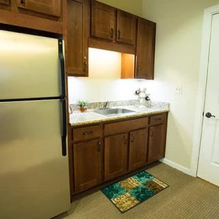 Compact apartment kitchen with wooden cabinets and a stainless steel fridge.