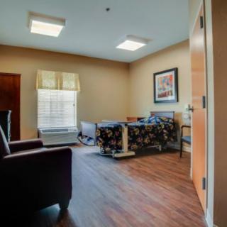 A healthcare facility room with a bed, chair, and window.