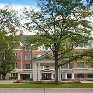 A large brick building with a grand entrance, framed by trees and situated along a street.