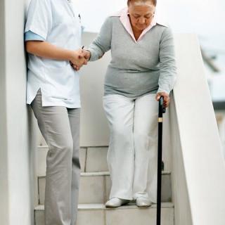 A caregiver assisting an elderly woman with a cane down the stairs.