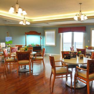 A well-lit dining area featuring multiple tables and chairs, with elegant lighting fixtures and hardwood flooring.