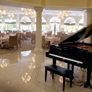 An elegant dining area with a grand piano and chandeliers.