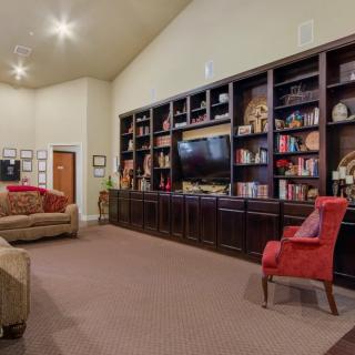 A cozy living room featuring a large shelving unit filled with books and decor, a television, comfortable seating options including a couch and an armchair, and soft carpeted flooring.
