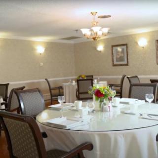 A formal dining room with a round table set for a meal, featuring elegant chairs, a floral centerpiece, and ambient lighting.