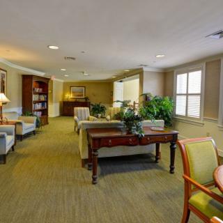 A cozy and well-furnished living room with sofas, chairs, a bookshelf, and indoor plants.