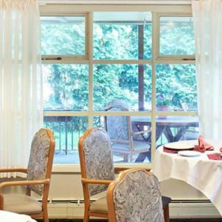 A bright dining area with chairs and a table set near a large window overlooking an outdoor space.