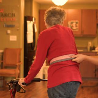 An elderly person is being assisted while using a walking aid in an indoor setting.