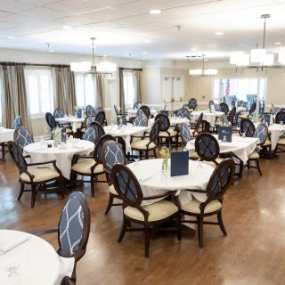 A spacious dining room with elegantly set tables and chairs, featuring white tablecloths and chandeliers.