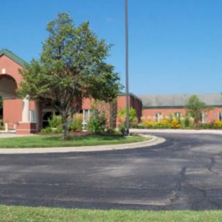 A brick building with a roundabout driveway and surrounding trees and landscaping.