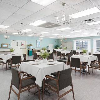 A bright and clean dining room set with tables and chairs, featuring chandeliers and natural light.