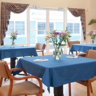 A well-lit dining area with blue tablecloths and flower arrangements.