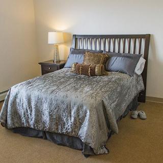 A neatly made bed in a cozy bedroom with a bedside lamp.