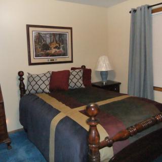A cozy bedroom featuring a wooden bed with colorful bedding, artwork on the wall, and a lamp on a bedside table.