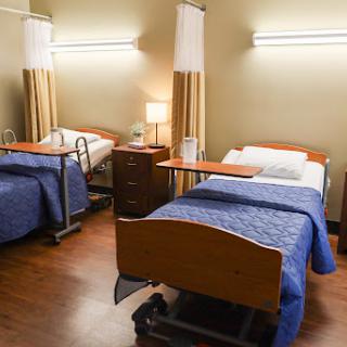 A view of a hospital patient room with two beds and essential furniture.