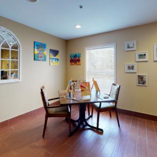 A cozy dining area with a round table, chairs, and colorful artwork on the walls.