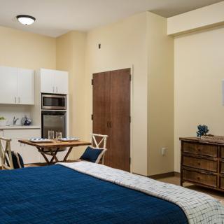 A modern studio apartment featuring a cozy bedroom area, compact kitchen, and dining table.