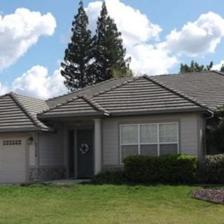 A single-story suburban house with a manicured front yard and trees in the background under a cloudy sky.
