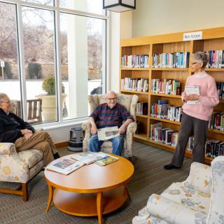 A group of people having a discussion in a library setting with bookshelves in the background.