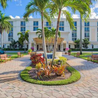 A sunny view of a landscaped area with palm trees and benches in front of a modern building.
