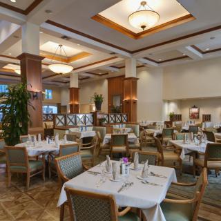 An elegant restaurant dining area with neatly arranged tables and chairs, featuring chandeliers and tasteful decor.