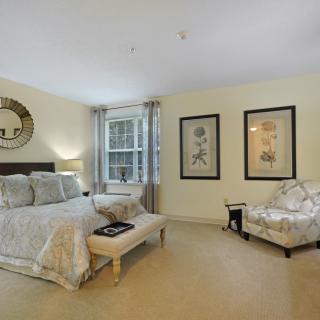 A cozy, well-decorated bedroom featuring a bed with patterned linens, a comfortable chair, and framed artwork on the walls.