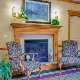 A cozy indoor setting with a fireplace, two ornate chairs, and decorative elements including a painting and plants.