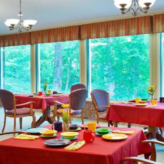 A bright dining room with red tablecloths and large windows overlooking a green landscape.