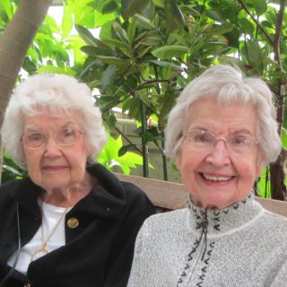 Two elderly women enjoying a day outdoors amidst greenery.
