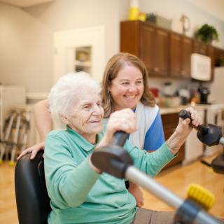 An elderly woman exercising with the support of a caregiver.