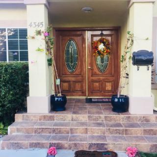 A welcoming front porch with wooden double doors, decorated with a wreath and flanked by potted plants.