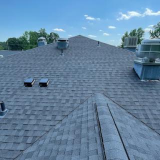 A view of a residential roof featuring gray shingles and ventilation structures against a clear blue sky.
