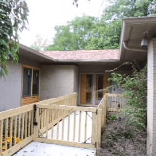 A house exterior with a wooden ramp surrounded by trees.