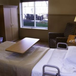 A hospital room with a bed, chair, and table near a window.
