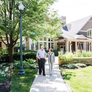 Two people walking on a pathway outside a building surrounded by greenery.