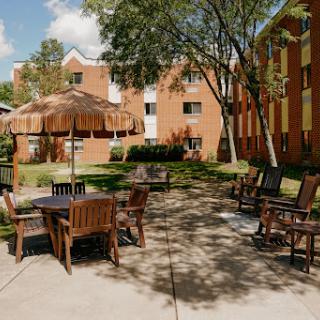 A cozy outdoor courtyard area featuring wooden furniture and a large umbrella, surrounded by apartment buildings and lush greenery.
