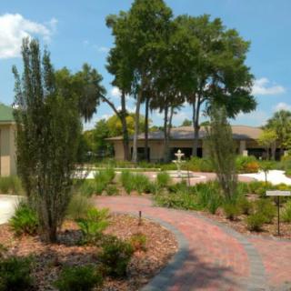 A serene garden with a brick pathway and lush greenery leading to a building.