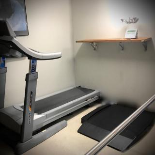 A minimalist fitness room featuring a treadmill and a small shelf.