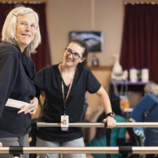 A therapist assists an elderly woman during a physical therapy session.