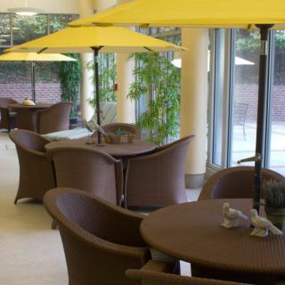 An indoor cafe area with tables and chairs, featuring yellow umbrellas and large windows.