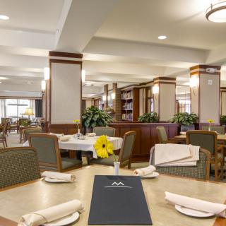 A well-lit dining area with neatly set tables and chairs, featuring elegant decor and modern lighting.