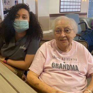 An elderly woman sitting next to a caregiver who is wearing a mask.